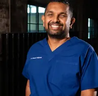 Dr Dinesh Palipana in blue scrubs, smiling.