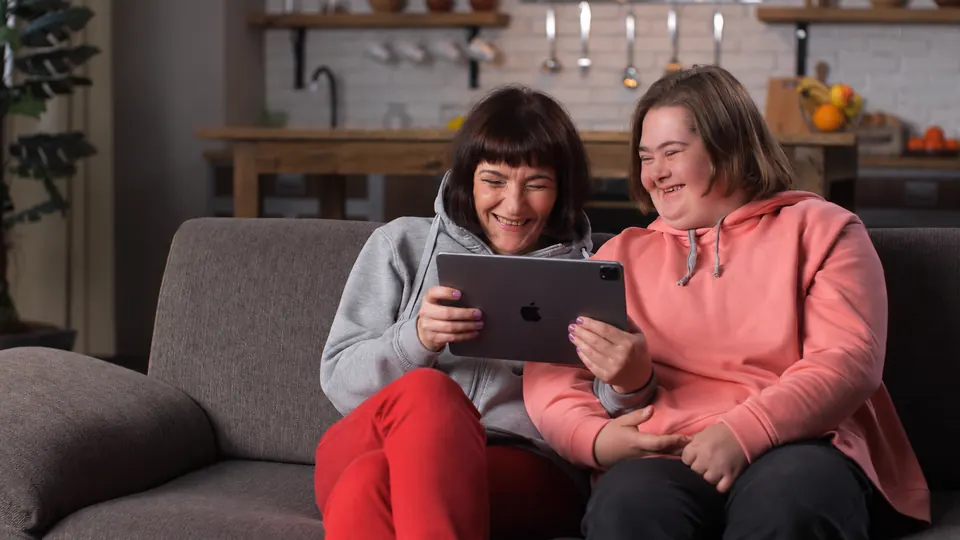 Two friends on a sofa, laughing together at an iPad.