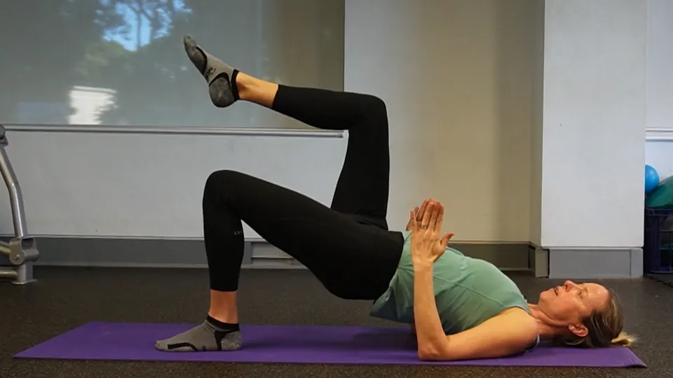 A woman doing a glute bridge on a mat, from an Able video.